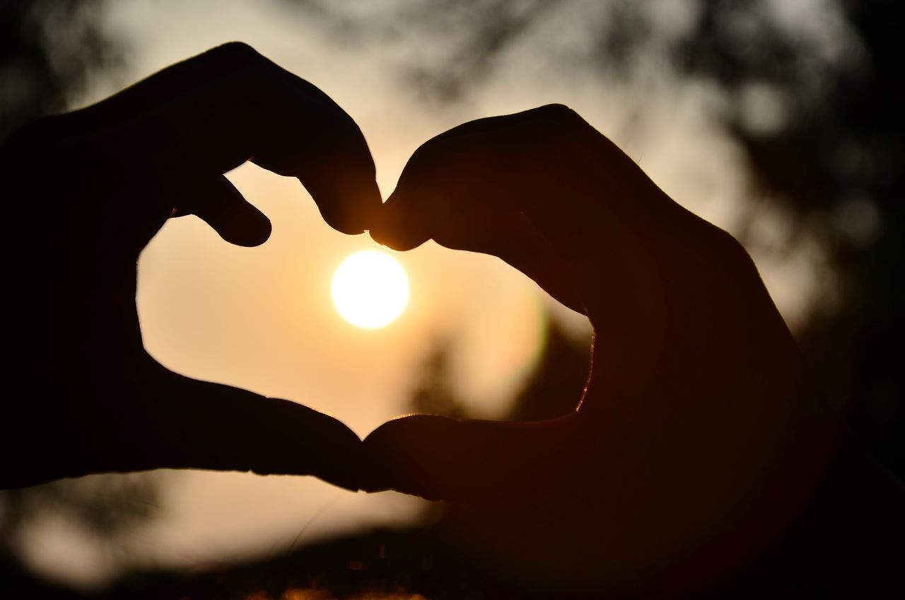 Crafting Captivating Headlines: Your awesome post title goes here Silhouette of hands forming a heart shape around a glowing sunset outdoors.