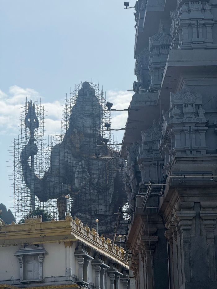 Services A colossal Shiva statue under maintenance against a bright sky.